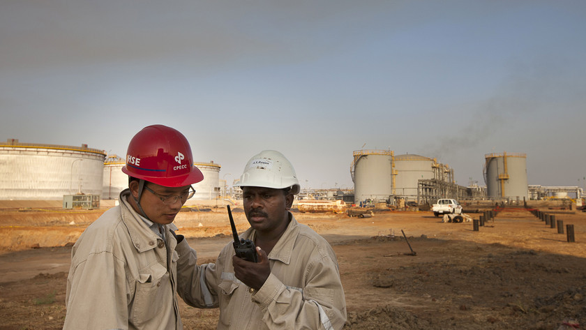 Workers for China Petroleum Engineering & Construction Corp. (CPECC) talk on a mobile handset by oil storage tanks near Melut, in the Upper Nile, Sudan.Photographer: Trevor Snapp/Bloomberg