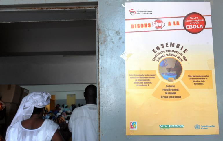 People stand in town hall of Les Parcelles Assainies district in Dakar where is posted an Ebola prevention poster on September 11, 2014. The country has managed to stave off the Ebola outbreak that has hit many of its west African neighbors