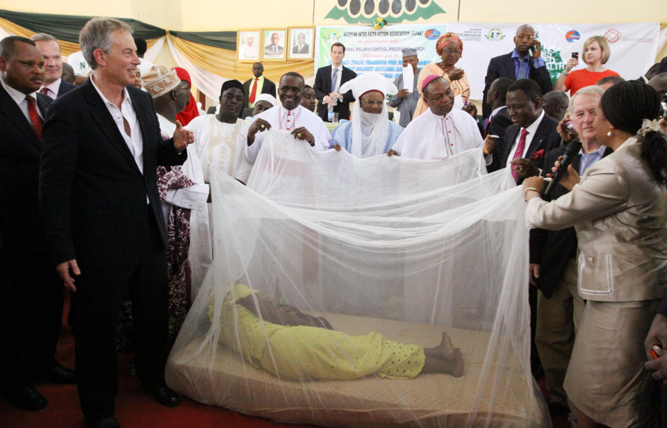FILE- In this Saturday, Feb. 20, 2010, file photo, former British Prime Minister Tony Blair, left, former Nigerian President Olusegun Obasanjo, on Blair's left, and Religion Leaders hold a Mosquito net with a women lying inside to demonstrate the use of the net against malaria in Abuja, Nigeria. The operation to fight Ebola in West Africa has hampered the campaigns against malaria, a preventable and treatable disease that is claiming many thousands of lives. In information released Sunday Dec. 28, 2014, Dr. Bernard Nahlen, deputy director of the U.S. President’s Malaria Initiative says they have had to stop pricking fingers to do blood tests for malaria, so statistics show a decrease in reported cases of maleria but the decrease is likely because people are too scared to go to health facilities and are not getting treated for malaria.(AP Photo/Sunday Alamba, FILE)