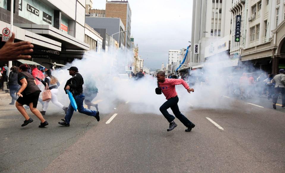 People run for cover from a stun grenade and tear gas after a skirmish between locals and foreign nationals as thousands of people take part in the "peace march" against xenophobia in Durban, South Africa, on April 16, 2015 (AFP Photo/)