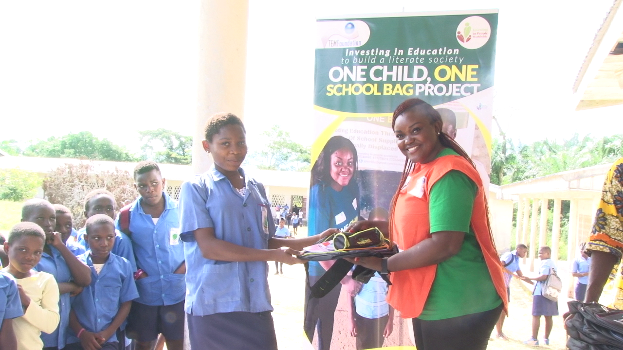 Ruth Besong, Executive Director of IPW hands school material to a Child at the Government Secondary School Mudeka