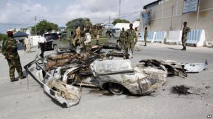 Somali soldiers stand near the wreckage of car bomb that was detonated at the main gate of the presidential palace in Mogadishu, July, 9, 2014.