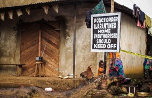 A child, center, stands next to a signboard reading 'Police order quarantined home unauthorised should keep off' as a family home is placed under quarantine due to the Ebola virus in Port Loko, Sierra Leone, Wednesday, Oct. 22, 2014. U.S. authorities said Wednesday that everyone traveling into the U.S. from Ebola-stricken nations will be monitored for symptoms for 21 days. That includes returning American aid workers, federal health employees and journalists, as well as West African travelers. The program will start Monday in six states that represent 70 percent of people arriving from Liberia, Sierra Leone and New Guinea, said the Centers for Disease Control and Prevention. (AP Photo/ Michael Duff)