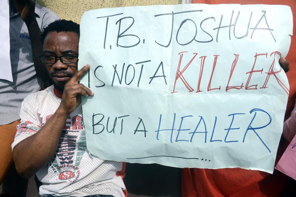 A man holds a placard to protest the coroner's inquest on October 30, 2014 at the Ikeja High Court in Lagos into the cause of the collapse at a guesthouse of the Synagogue Church of All Nations, led by TB Joshua (AFP Photo/Pius Utomi Ekpei)