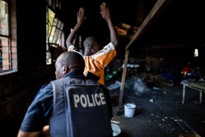 A resident raises his hands as a South African anti-riot police officer raids a hostel in Benoni on April 16, 2015 (AFP Photo/Marco Longari)